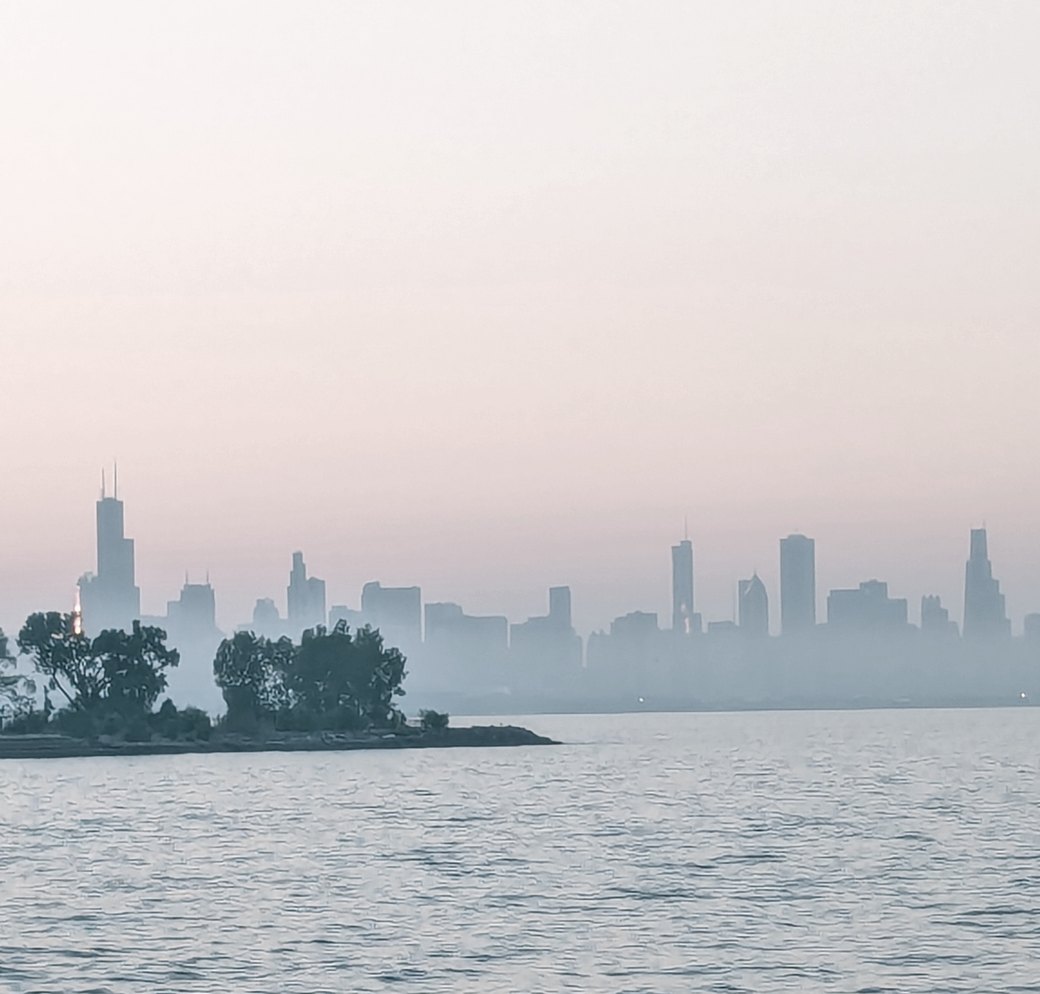 The Chicago skyline at dawn, seen across Lake Michigan through haze.