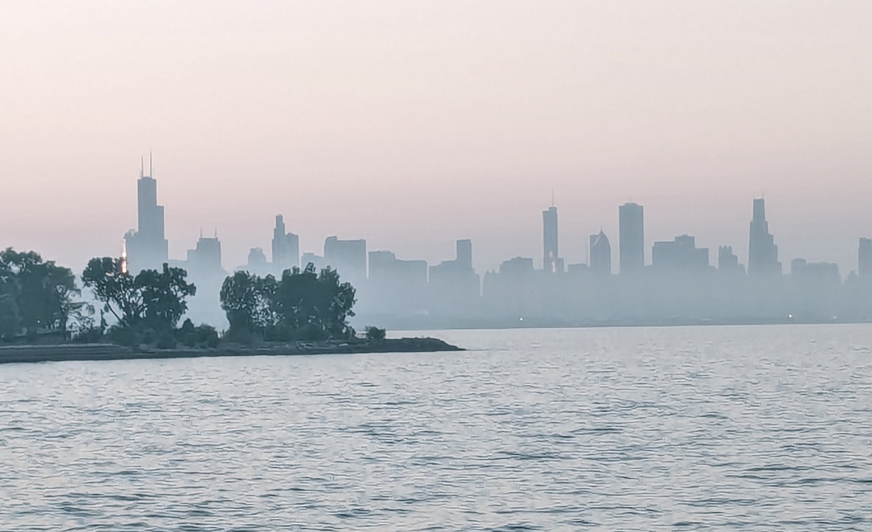 The Chicago skyline at dawn, seen across Lake Michigan through haze.